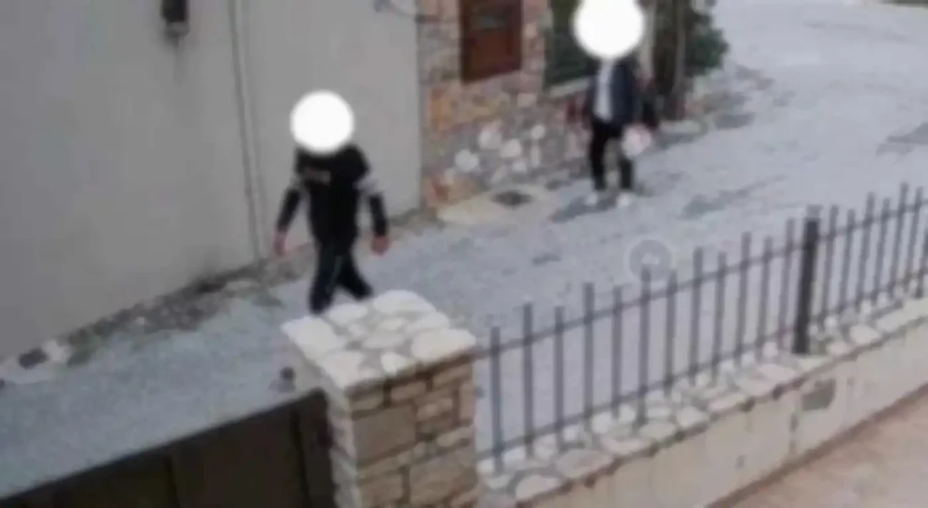 Καθώς οι δύο φιγούρες προχωρούν, η σκιά τους μακραίνει πάνω στους πέτρινους τοίχους σαν να τους ακολουθεί κάτι αόρατο.