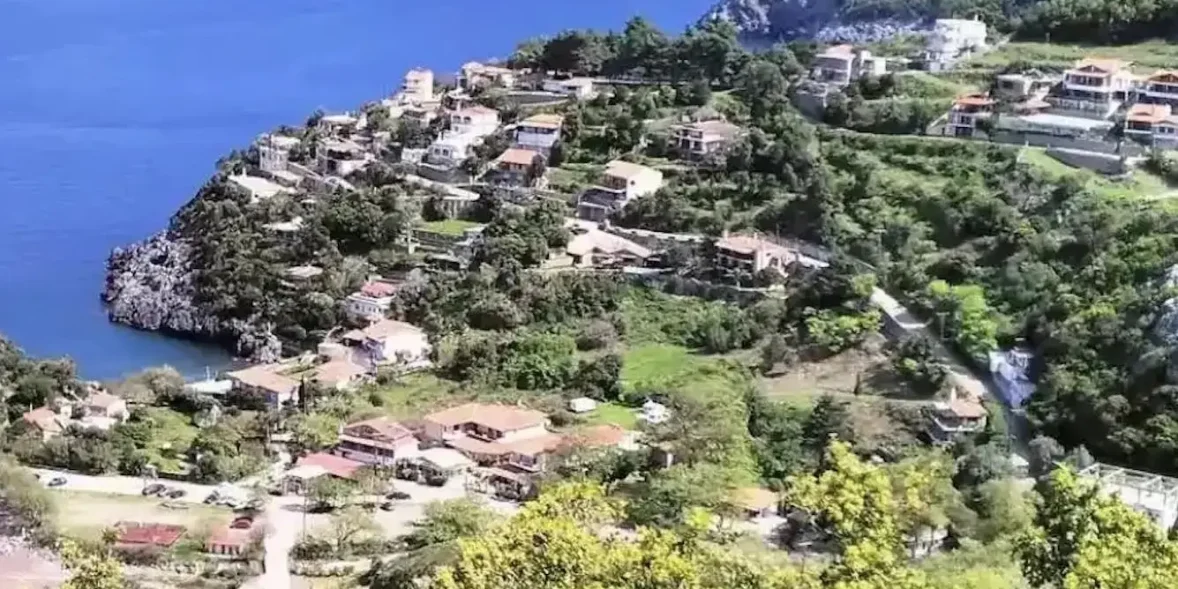 Πανοραμική θέα της Αγίας Σοφίας στην Εύβοια, με καταπράσινες πλαγιές, σπίτια με κεραμοσκεπές και στο βάθος το ρέμα που κατηφορίζει προς τον Λιμνιώνα. Ήπιο απογευματινό φως και καθαρός ουρανός.