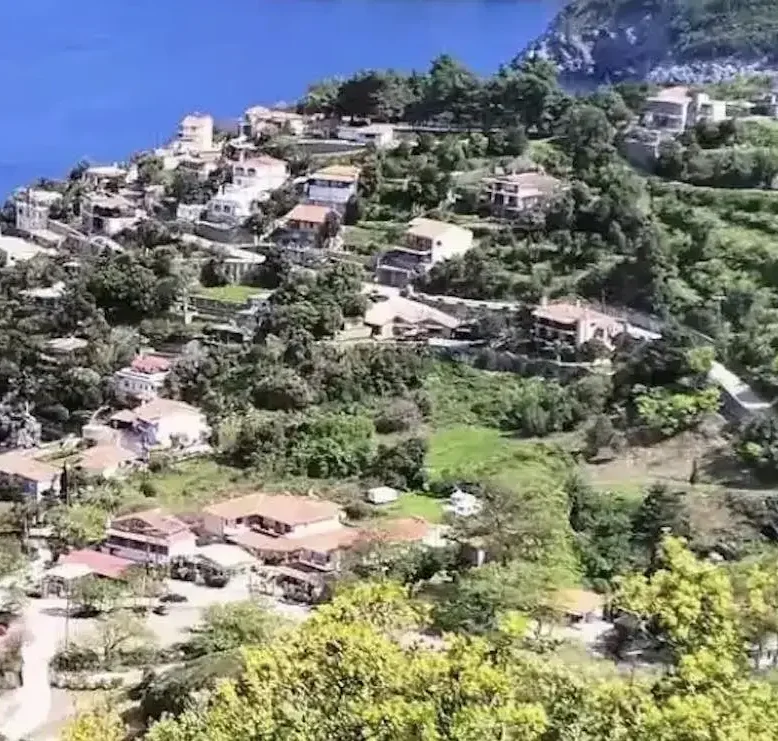 Πανοραμική θέα της Αγίας Σοφίας στην Εύβοια, με καταπράσινες πλαγιές, σπίτια με κεραμοσκεπές και στο βάθος το ρέμα που κατηφορίζει προς τον Λιμνιώνα. Ήπιο απογευματινό φως και καθαρός ουρανός.